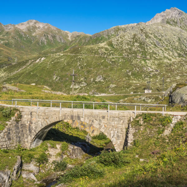 Steinbrücke über die Gotthardreuss mit Alpenlandschaft im Hintergrund.