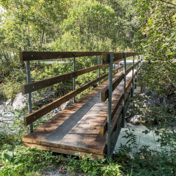 Holzbrücke über den Grassenbach, umgeben von grüner Vegetation.