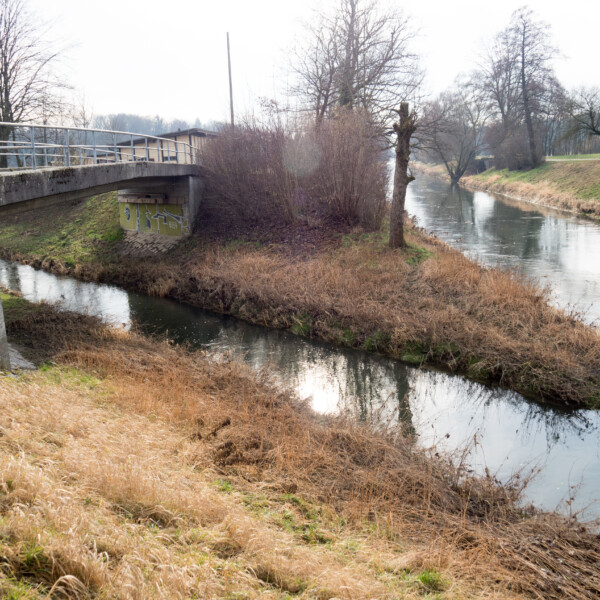 Brücke über den Himmelbach mit Uferbewuchs und Bäumen im Hintergrund.