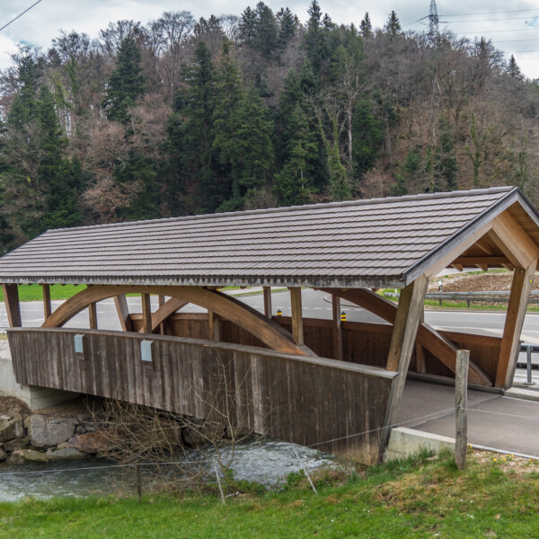 Gedeckte Holzbrücke über die Hintere Frenke, eingebettet in grüne Landschaft.