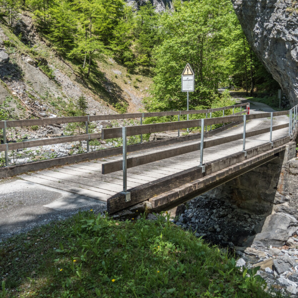 Holzbrücke über den Limmerenbach mit Warnschild vor felsiger Landschaft.