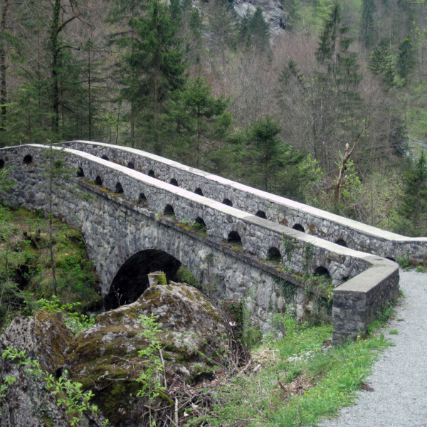 Alte Steinbrücke über den Löntsch in bewaldeter Landschaft.