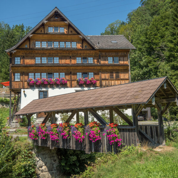 Gedeckte Brücke mit Blumen vor einem Holzhaus in Lütisbach.
