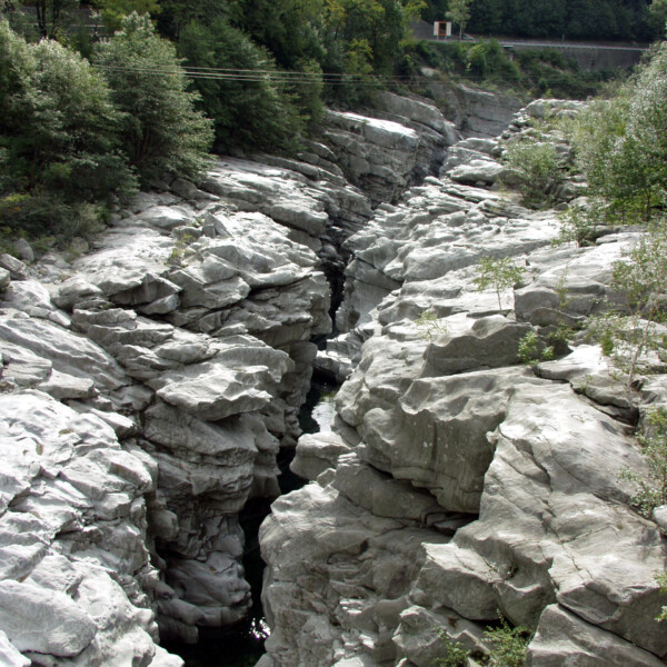 Grauer Felsenschlucht im Maggiatal mit Wasserlauf und Bäumen.