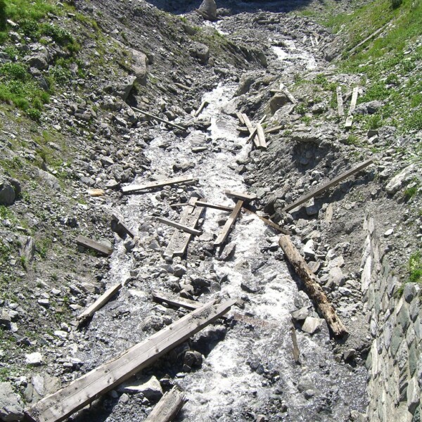Geröllhalde mit Bachlauf und Holzresten. Natürliche Landschaft.