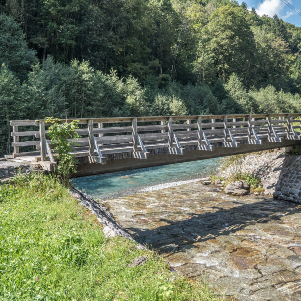 Holzbrücke über den Bach in Mühlebach (Engi) mit grüner Umgebung.
