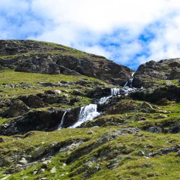 Wasserfall am Ovel da Languard, eingebettet in grüne Berghänge unter blauem Himmel.