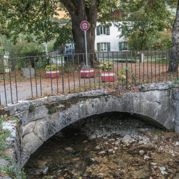 Steinbrücke über Bach mit Baum und Verbotsschild im Hintergrund. Herbstliche Landschaft.