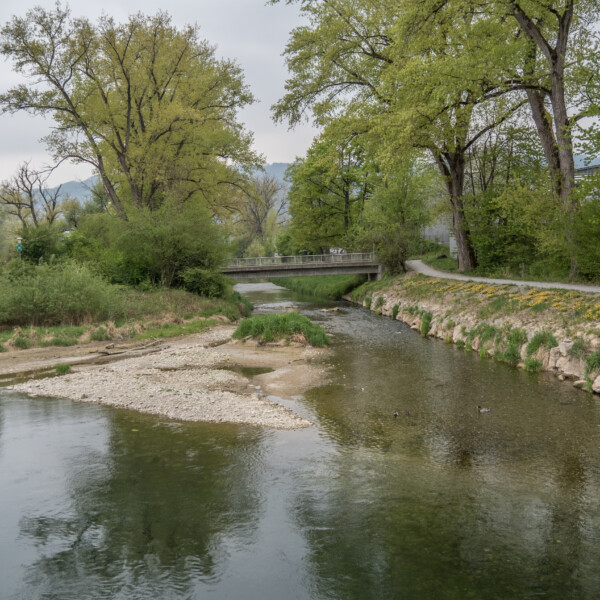 Fluss Reppisch mit Brücke, Bäumen und Uferlandschaft im Frühling.