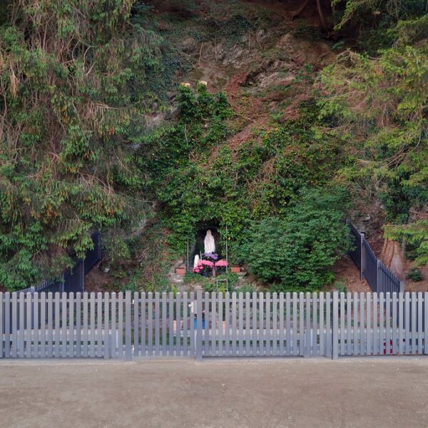 Marienstatue in einer Grotte im Saarland, umgeben von Grün und einem grauen Zaun.