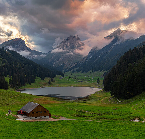 Sämtisersee mit Hütte, grünen Wiesen und Bergen unter bewölktem Himmel.