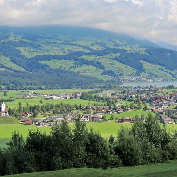 Sarnersee-Panorama mit Dorf, Kirche und grünen Hügeln in der Schweiz.