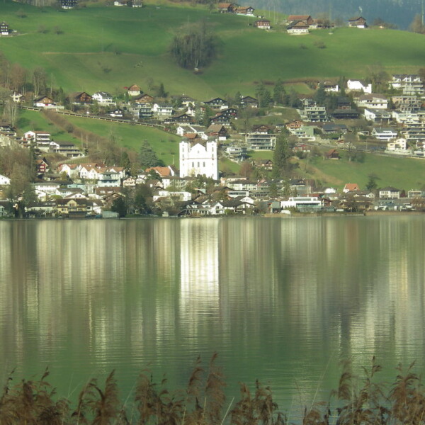 Sarnersee-Ansicht mit Häusern am Hang und Spiegelung im Wasser.
