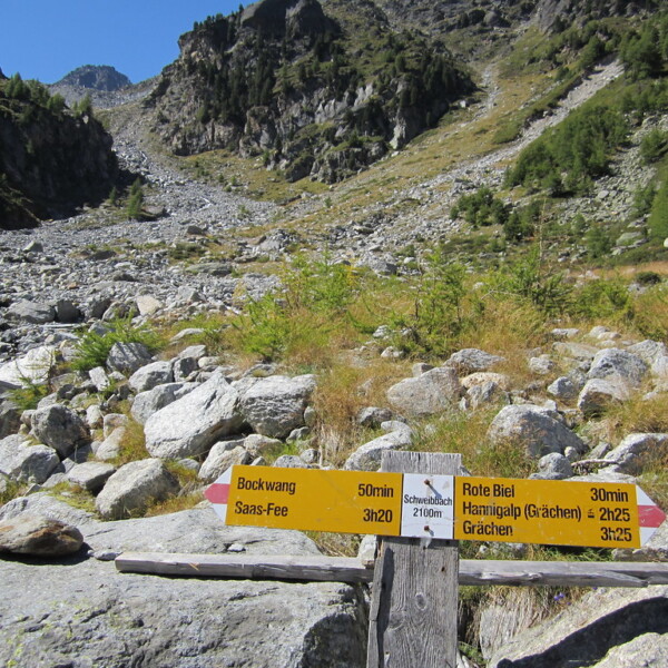 Wegweiser in Schweibbach, Saas-Fee, mit Zielen wie Bockwang, Rote Biel und Hannigalp. Wanderweg in den Bergen.