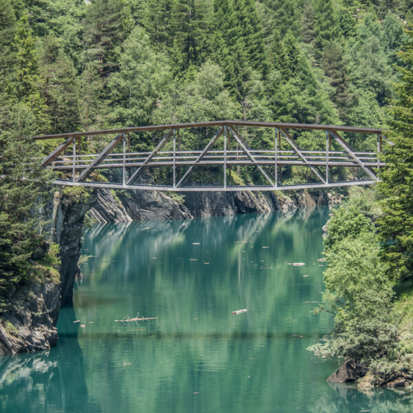 Brücke über Lai da Seara mit türkisblauem Wasser und grünen Bäumen.