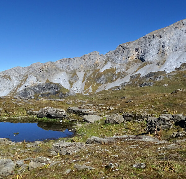 Seelenen: Bergsee in alpiner Landschaft mit markantem Felsmassiv unter blauem Himmel.