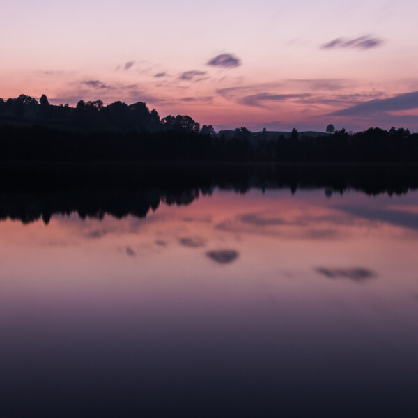 Soppensee bei Sonnenuntergang: Stille Wasser spiegeln den violetten Himmel und die Bäume.