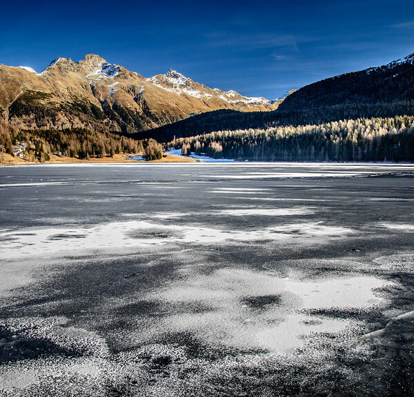 Gefrorener St. Moritzersee mit Bergen im Hintergrund unter blauem Himmel.