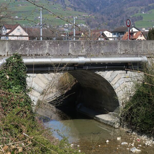 Brücke über den Stadtbach in Altstätten, Schweiz. Fluss unter Betonbogen, grüne Landschaft im Hintergrund.