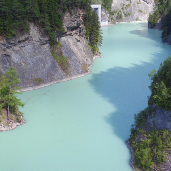 Stausee Solis: Türkisblauer Stausee umgeben von Felsen und Bäumen.