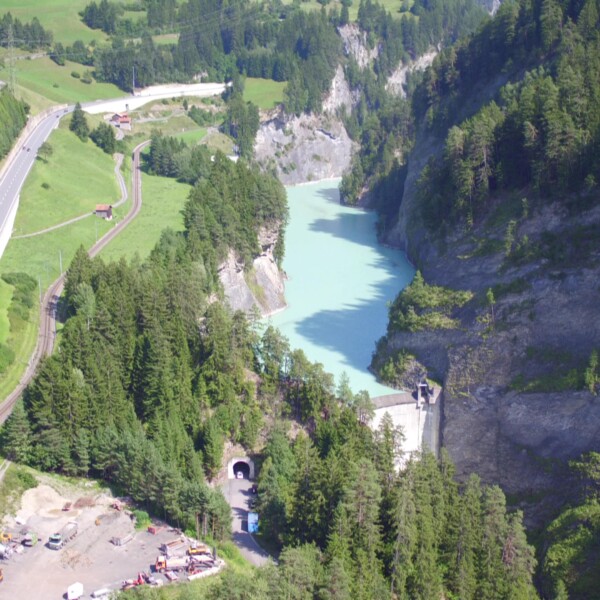 Stausee Solis: Luftaufnahme von Stausee, Straße und Tunnel in grüner Landschaft.