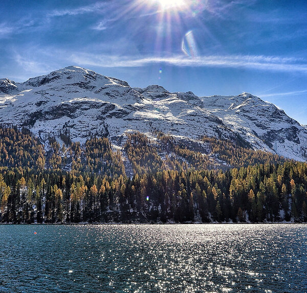 Stazersee mit Bergen, Wald und blauem Himmel. Sonnenschein reflektiert im Wasser.