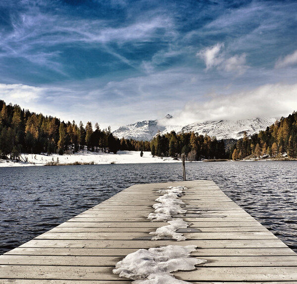 Steg am Stazersee mit Blick auf See, Wald und schneebedeckte Berge