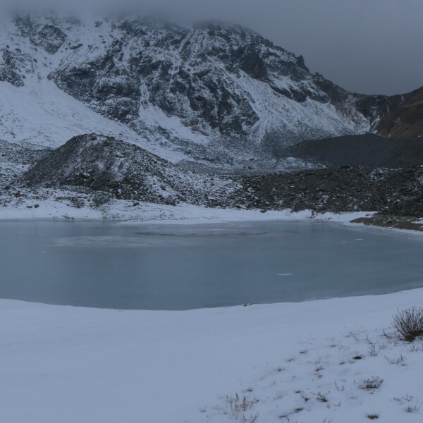 Gefrorener Tambosee in verschneiter Berglandschaft.