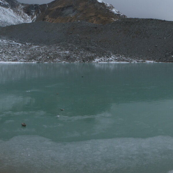 Teilweise gefrorener Tambosee in hochalpiner Landschaft mit Schnee und Geröllhalden.