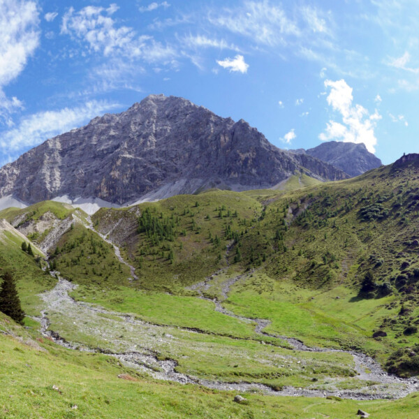 Tiejerbach: Berglandschaft mit grünen Wiesen und felsigem Gipfel unter blauem Himmel.