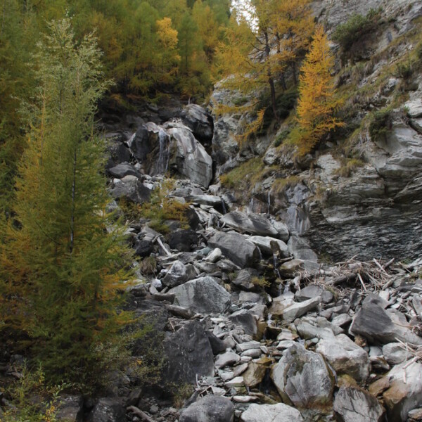 Triftbach Wasserfall in Zermatt mit Felsen und herbstlichen Bäumen.