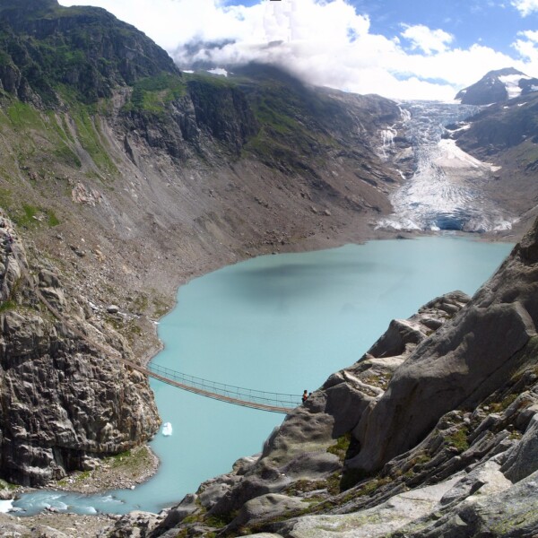 Triftsee-Hängebrücke mit türkisfarbenem Gletschersee und Bergen in der Schweiz.