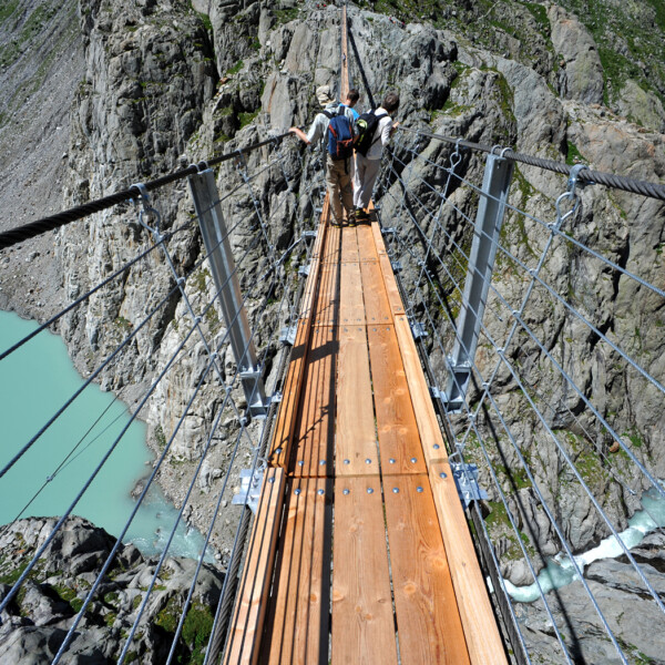 Wanderer auf der Triftbrücke über den türkisfarbenen Triftwasser-See in den Schweizer Alpen.