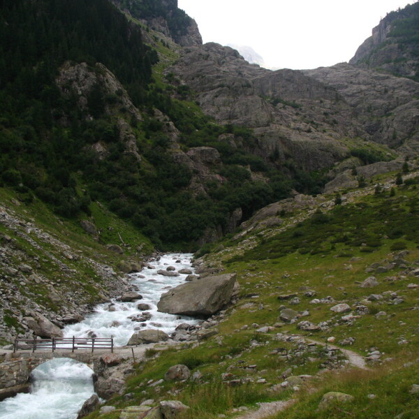 Fluss Triftwasser mit Steinbrücke in alpiner Landschaft