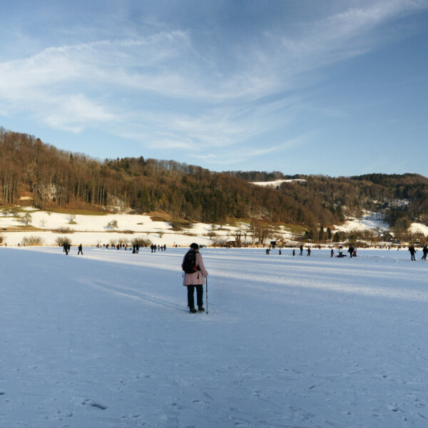 Türlersee im Winter: Menschen auf dem zugefrorenen See mit Hügeln im Hintergrund.