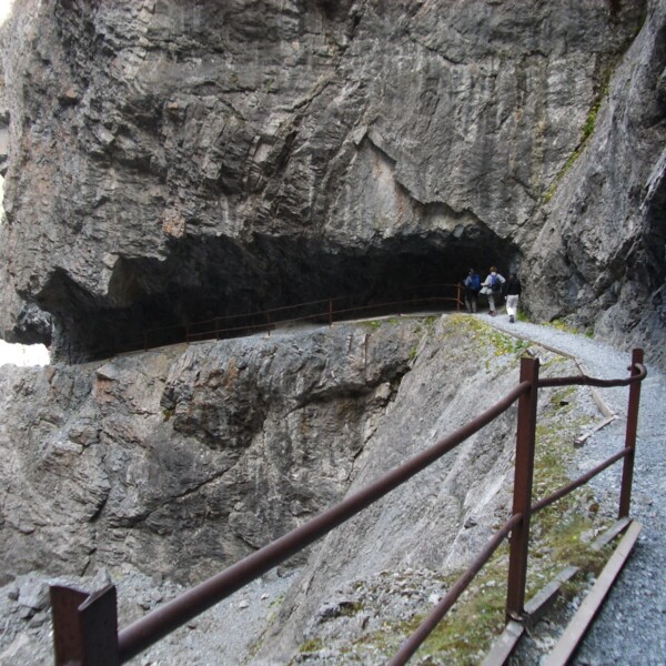 Uina Schlucht: Wanderweg mit Geländer durch Felsen. Zwei Wanderer im Hintergrund.
