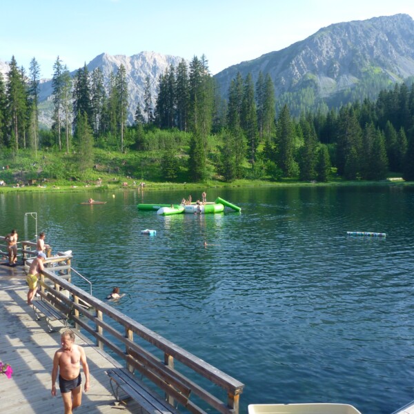 Untersee Arosa: Badegäste genießen den Sommer an einem Bergsee mit bewaldeten Ufern und Bergen im Hintergrund.