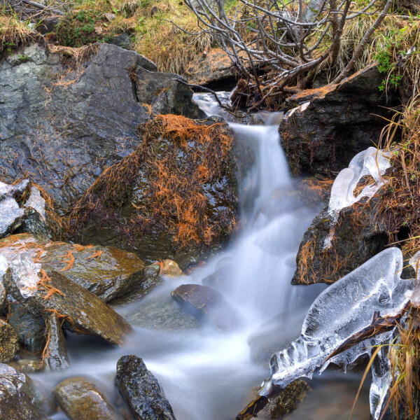 Fließender Bach in Val da Camp, umgeben von Felsen und Eis.