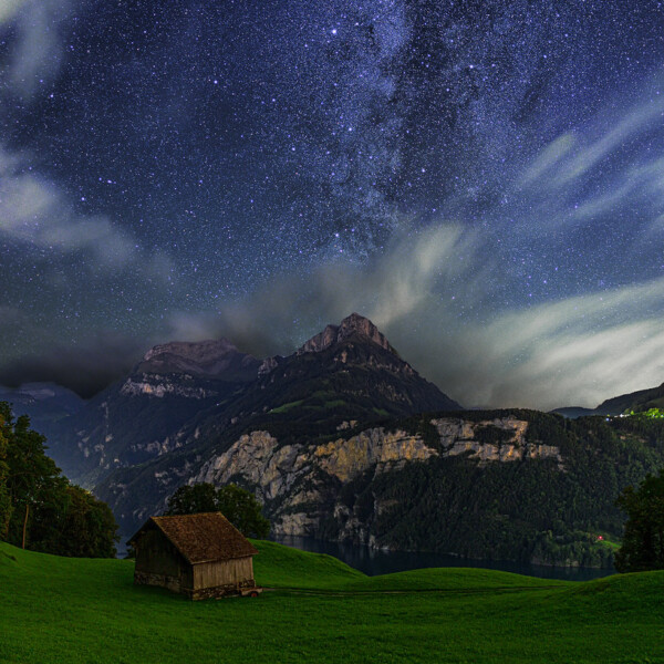 Sternenhimmel über dem Vierwaldstättersee mit Bergen und einer Hütte auf grüner Wiese.