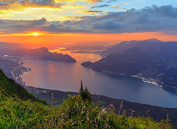 Sonnenuntergang über dem Vierwaldstättersee mit Bergen und grüner Landschaft im Vordergrund.