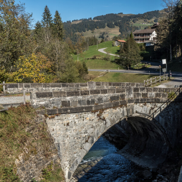 Steinbrücke über die Warme Sense in einer grünen Landschaft mit Häusern im Hintergrund