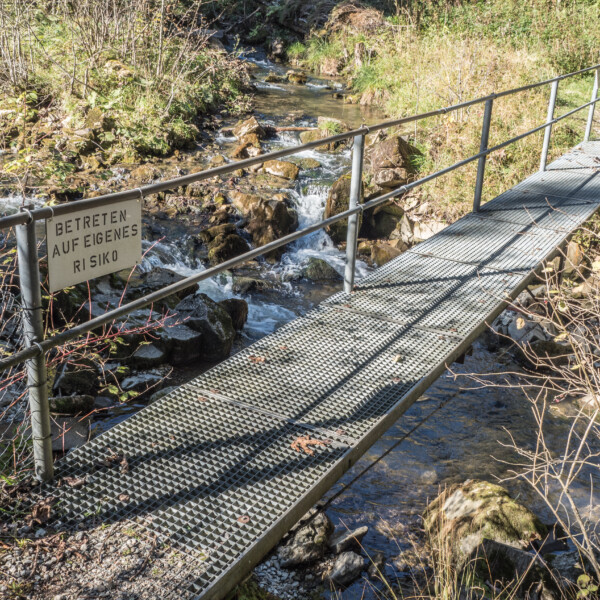 Metallbrücke über Bach mit Warnschild 