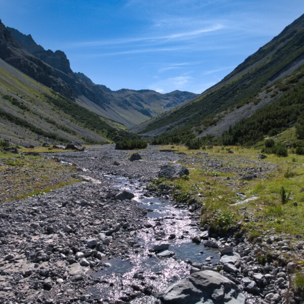 Welschtobelbach: Bachlauf durch alpines Tal mit Bergen und blauem Himmel.