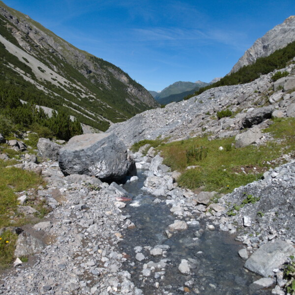 Welschtobelbach Gebirgsbach mit Felsen und grünen Hängen unter blauem Himmel.