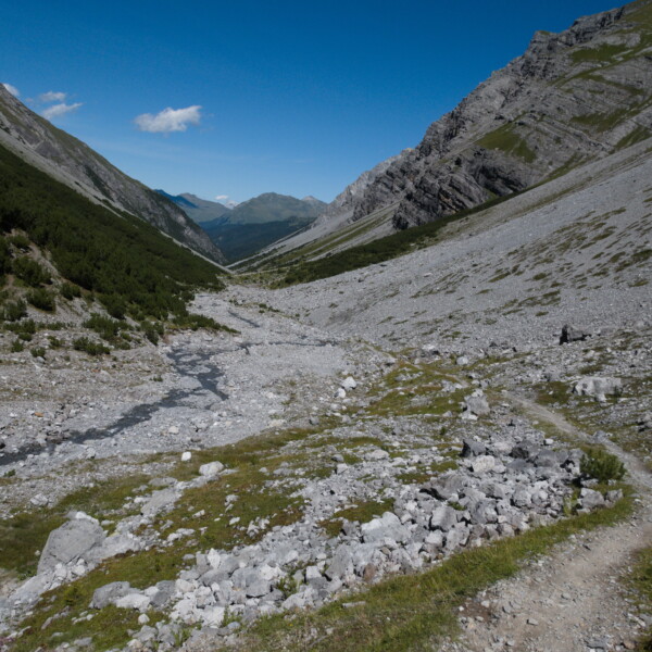 Tal im Welschtobelbach mit Geröllfeld und Wanderweg unter blauem Himmel.