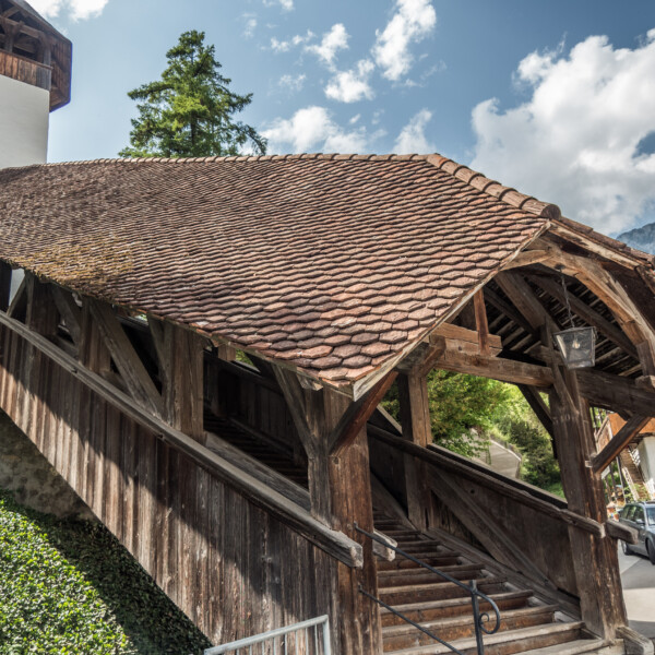 Gedeckte Holzbrücke in Wildenbach mit Ziegeldach und Uhr an einem Gebäude.
