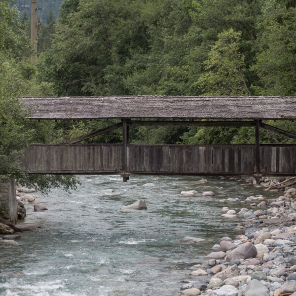 Gedeckte Holzbrücke über den Fluss Albula, umgeben von Bäumen.