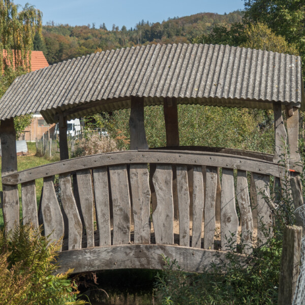 Überdachte Holzbrücke mit gewelltem Dach in Allaine.