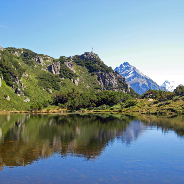 Arniseeli Bergsee mit Spiegelung der umliegenden Berge und Vegetation.