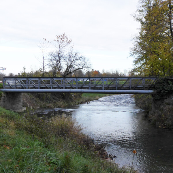 Metallbrücke über den Fluss Arnon, umgeben von Bäumen und Vegetation.